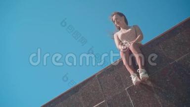 一个穿<strong>白色短裤</strong>和T恤的女孩沿着城市长廊。 一个女孩坐在花岗岩栅栏上。