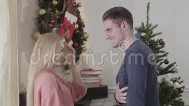 侧面观看快乐的白种人夫妇在家的圣诞树前欢笑和拥抱。 积极的家庭开支