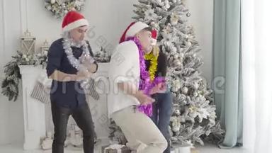 三个快乐的白种人朋友在装饰圣诞树前跳舞的肖像。 快乐的双胞胎兄弟