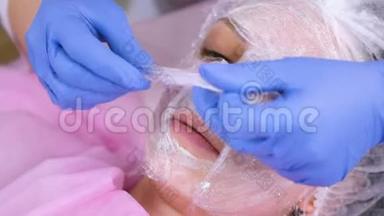 美容师把一层塑料薄膜贴在女士脸上的保湿面膜上面..
