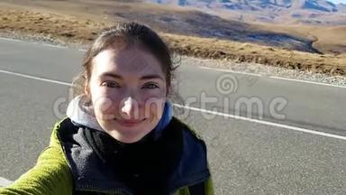 布鲁内特女孩旅行者在柏油路的背景下拍摄一张自拍。 前往俄罗斯
