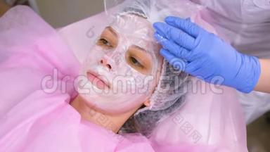 美容师把一张塑料薄膜贴在保湿面膜上面，贴在女人`脸上。