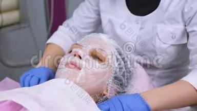 美容师从女人`脸上取出毛巾。 美容师从女人的<strong>保湿面膜</strong>上取出一层塑料膜