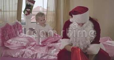穿着圣诞老人服装的白人男子坐在粉<strong>红</strong>色的床上，小女孩扎着<strong>辫子</strong>抚摸着他的肩膀