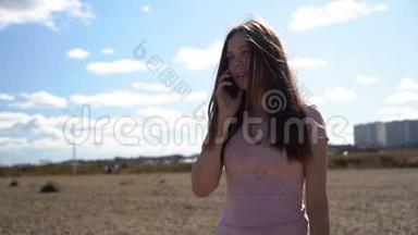 穿着粉色t恤和蓝色牛仔裤的漂亮女孩，或者在沙滩上走在木路上，用智能手机聊天的女人