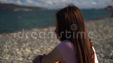 坐在沙滩上穿着<strong>粉色</strong>t恤的年轻女子或女孩的正面特写镜头看向别处，而不是对着镜头<strong>微</strong>笑