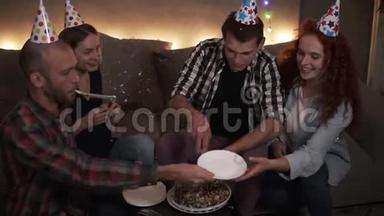 穿格子衬衫的生日人用五颜六色的锥形帽子剪生日蛋糕。 在圆锥体中快乐的朋友
