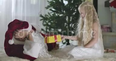 快乐的白人女孩，卷发，送礼物给穿圣诞老人服装的男人。 可爱的儿童礼物