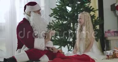 可爱的白种人女孩，穿着白色连衣裙，戴着皇冠，和圣诞老人坐在新年树前，给他<strong>击掌</strong>