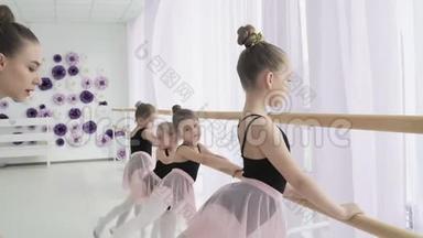 勤奋的年轻芭蕾舞演员正在做芭蕾舞和击球练习，而他们的女老师正在纠正错误