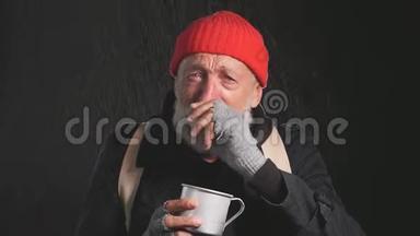 无家可归的老人穿着外套，戴着一顶红帽子，站在雨中，梦想着自己的庇护和哭泣。