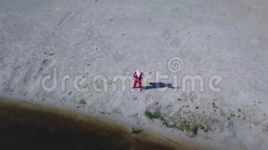 圣诞老人站在湖边的沙滩上，手里拿着一个礼品袋。 圣诞老人挥动他的手`你好`相机。 <strong>顶级</strong>