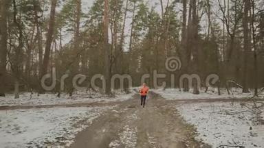 公园里的运动员训练。 精力充沛的女人穿着橙色夹克和蓝色腿在冬天的森林里晨跑。 职业介绍所