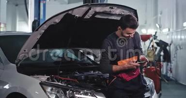 一个穿制服的工人微笑着在汽车修理厂修理汽车时看了看手机