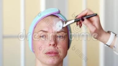 化妆师在化妆前`女孩的脸涂上保湿面膜。 手术在家里进行。