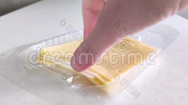 塑料包装中的方形黄色奶酪。 女白手拿一块.. 有小孔的切片奶酪