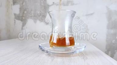 土耳其<strong>红茶</strong>倒入国杯.. 在透明杯和木桌上的茶托中特写棕色<strong>饮料</strong>。 琥珀