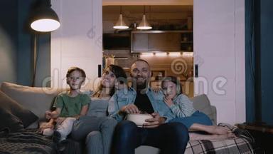 快乐微笑的年轻白种人家庭与两个孩子在家看电影沙发，一起笑。 娱乐概念。