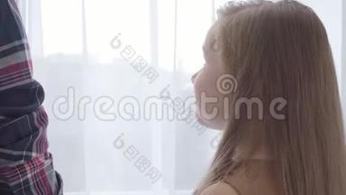 一个可爱的白人女孩的特写，长发，抬头看着不可辨认的男孩，看着窗外。 肖像