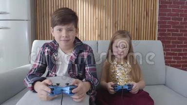 可爱的高加索儿童坐在沙发上玩电子游戏。 男孩离开，女孩做胜利的手势。 休闲