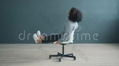 戏谑的非裔美国女孩在灰色背景的办公椅上旋转的肖像