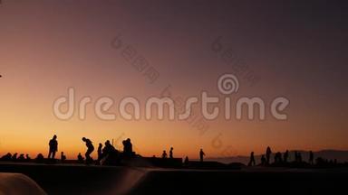 少年跳滑板的剪影骑长板，夏日夕阳背景.. 洛斯威尼斯海滨溜冰场