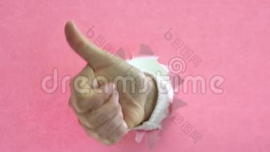女人的手在撕破的粉红纸背景上竖起大拇指。