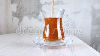 土耳其红茶倒入国杯.. 在透明杯和木桌上的茶托中特写棕色饮料。 琥珀