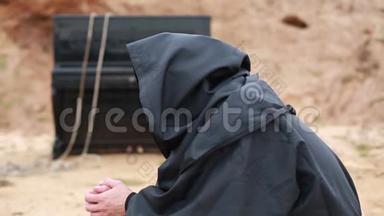 一个穿着黑袍带着头巾的<strong>和尚</strong>坐在空地上，在炉火旁取暖