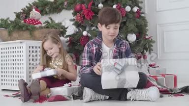 小男孩和小女孩拿着礼物<strong>坐在</strong>新年<strong>树下</strong>。 圣诞前夜快乐儿童的肖像。 假期