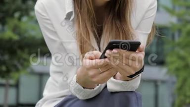 女人坐在公园的长凳上，在手机里输入一条信息。 <strong>特写双手</strong>。