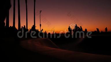 少年跳滑板的剪影骑长板，夏日夕阳背景.. 洛斯威尼斯海滨溜冰场