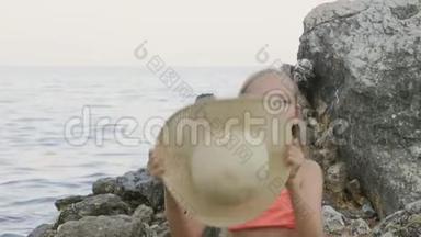 可爱的少年女孩穿比基尼在海水中的石头上戴草帽。 在海水中戴着夏帽的美女肖像