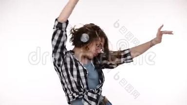 穿格子衬衫的年轻女子听着音乐，用耳机站在孤立的白色背景上，非常高兴和高兴