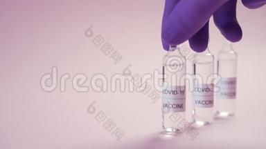 冠状病毒疫苗。 一只手戴着蓝色防护医疗手套，在粉红色的表面上拿起安瓿