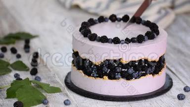 女人的手在切蛋糕。 紫色美丽的蛋糕，装饰着浆果，黑莓和蓝莓。
