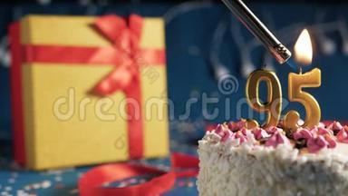 白色生日蛋糕数字95金蜡烛用打火机燃烧，蓝色背景灯和礼品黄色盒子用红色系起来