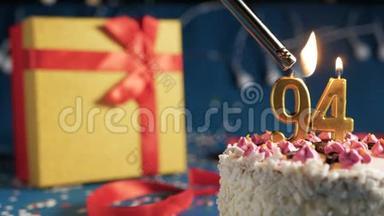 白色生日蛋糕编号<strong>94</strong>金色蜡烛由打火机燃烧，蓝色背景灯和礼品黄色盒子与红色捆绑