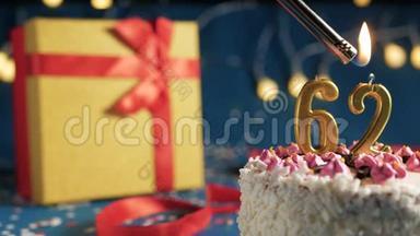 白色生日蛋糕数字62金蜡烛用打火机燃烧，蓝色背景灯和礼品黄色盒子用红色系起来