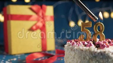 白色生日蛋糕编号58金色蜡烛用打火机燃烧，蓝色背景灯和礼品黄色盒子用红色系起来