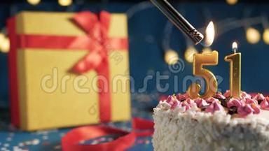 白色生日蛋糕编号<strong>51</strong>金色蜡烛由打火机燃烧，蓝色背景灯和礼品黄色盒子捆绑