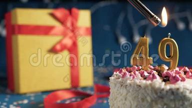 白色生日蛋糕数字49金蜡烛点燃打火机，蓝色背景灯和礼品黄盒子捆绑