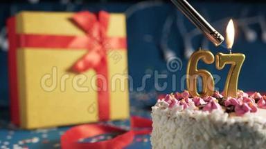白色生日蛋糕数字67金蜡烛由打火机燃烧，蓝色背景灯和礼品黄色盒子与红色捆绑