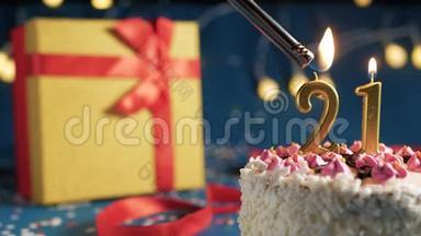 白色生日蛋糕21号金色蜡烛用<strong>打火</strong>机点燃，蓝色背景灯和礼品黄色盒子系好