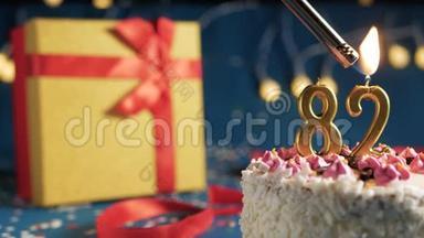 白色生日蛋糕82号金色蜡烛用打火机点燃，蓝色背景灯和礼品黄色盒子用红色系起来
