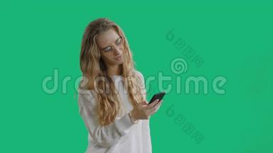 年轻漂亮的女士戴着时髦的眼镜，手里拿着一部智能手机，在绿色屏幕上使用智能手机
