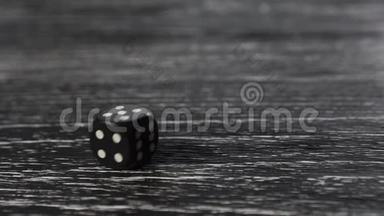 黑色骰子滚动，旋转和停止与数字5在顶部。 深色纹理的老式木制桌子