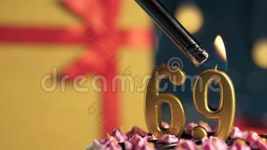 生日蛋糕数字69金色蜡烛用打火机点燃，蓝色背景礼品黄色盒子用红丝带绑好