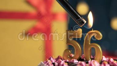 生日蛋糕数字56金色蜡烛用打火机点燃，蓝色背景礼品黄色盒子用红丝带系好