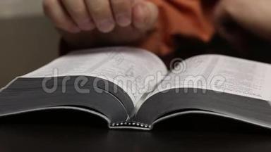 桌子上放着一本公开的圣经。 一个人读它，移动他的手指沿着线条，<strong>翻页</strong>。 特写镜头